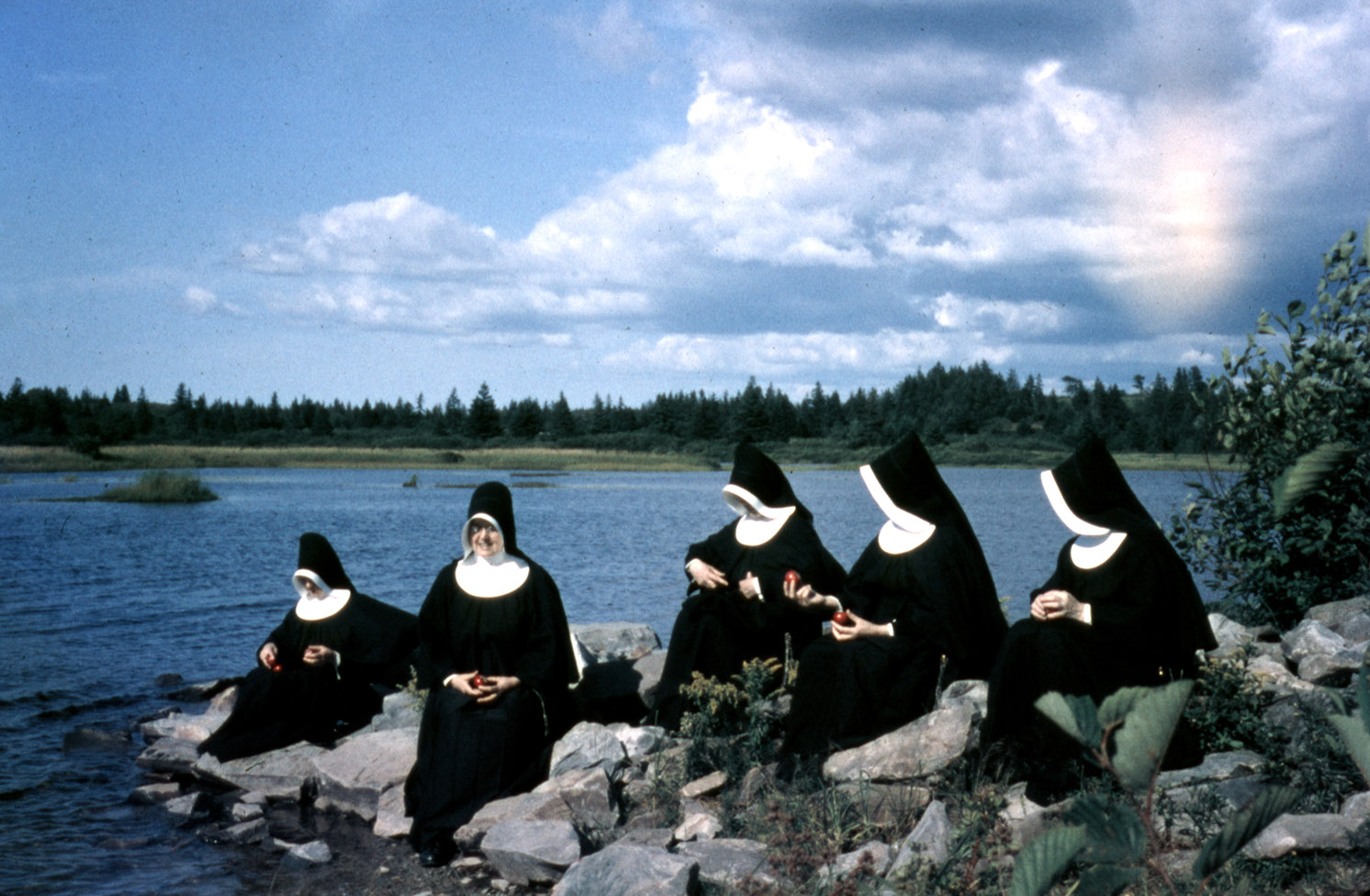 communityalbums - Sisters of Charity-Halifax sitting on rocks near water with red apples, Camp Monte Bello, Yarmouth, Nova Scotia.