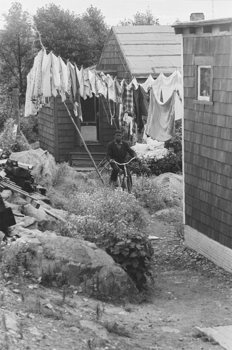 africville : Africville backyard scene, featuring a boy with his bicycle and a full clothesline of laundry  behind him