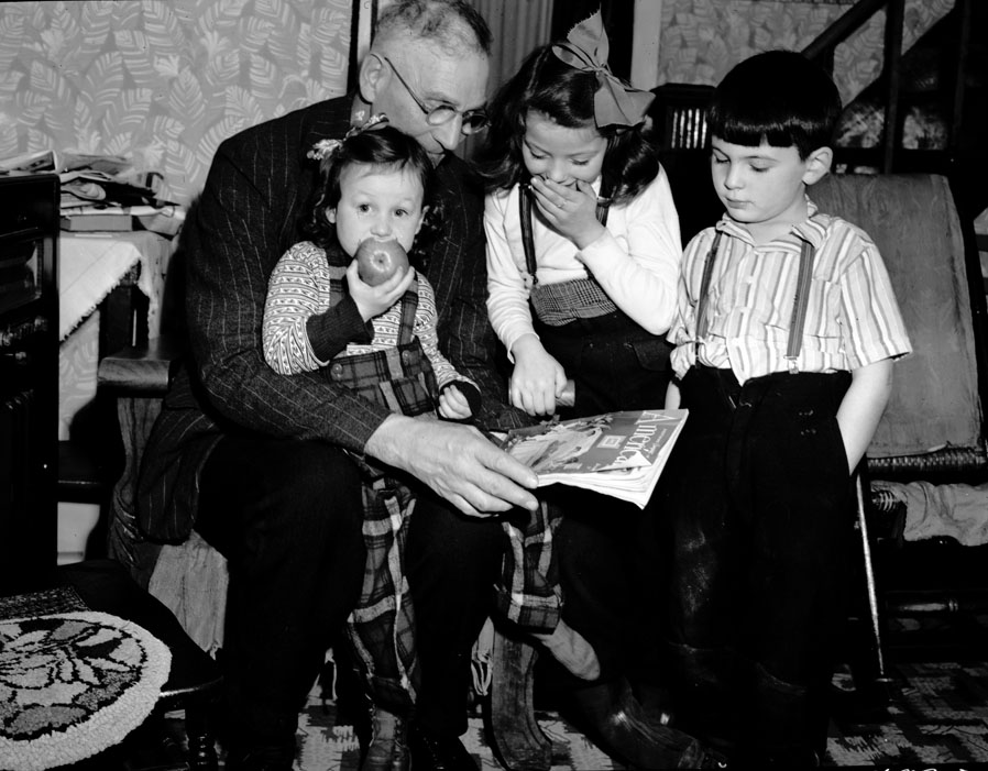 J. Vian Andrews entertains three of his grandchildren on Christmas night.  Children, left to right, Gail Andrews (Dean's daughter), Maxine Andrews (Reggie's daughter), and David Thomas (Phyllis's son). December 1950.