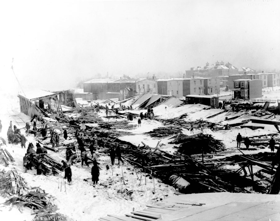 Collapsed buildings of Nova Scotia Car Works on Clifton Street near St. Albans Street, Halifax, with Bloomfield School in background at right, 11 February 1918